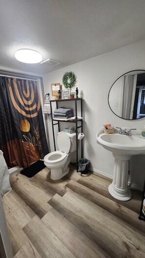 Een badkamer met een toilet, een wastafel, een plank met toiletartikelen, een douchegordijn en een spiegel.