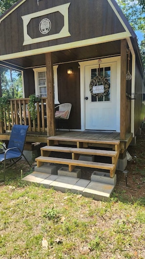 A wooden cabin with a porch, a welcome sign, and a bench.