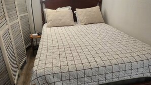 A neatly made bed with a quilted cover, a bedside lamp, and a wall with a framed sign and decorative wreaths. - The Dasher Den is a Cozy Tiny Cabin located right off of Highway 41 (Valdosta)