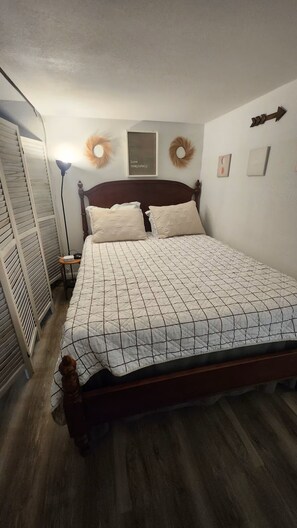 Een opgemaakt bed met een gewatteerde spreideken, een bedlampje en een muur met een lijst en decoratieve kransen.