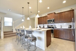 A modern kitchen with a central island, bar stools, wooden cabinets, stainless steel appliances, and pendant lighting. - Princess/StarWars 5-bedroom house in Orlando near Parks (Kissimmee)