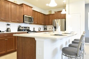 A modern kitchen with wooden cabinets, stainless steel appliances, and a central island with bar stools. - Princess/StarWars 5-bedroom house in Orlando near Parks (Kissimmee)