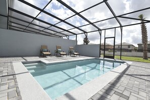 Una piscina con techo de vidrio, rodeada de sillones de descanso y un patio de ladrillo.