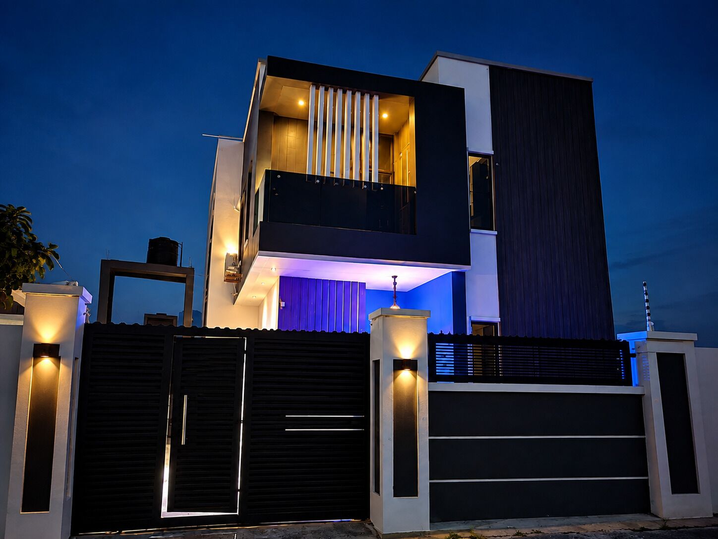 A modern two-story house with a balcony, a garage, and a gated entrance.