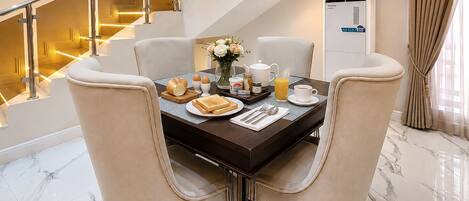 Un comedor con suelo de mármol, una mesa dispuesta con artículos para el desayuno y una escalera con barandilla dorada.