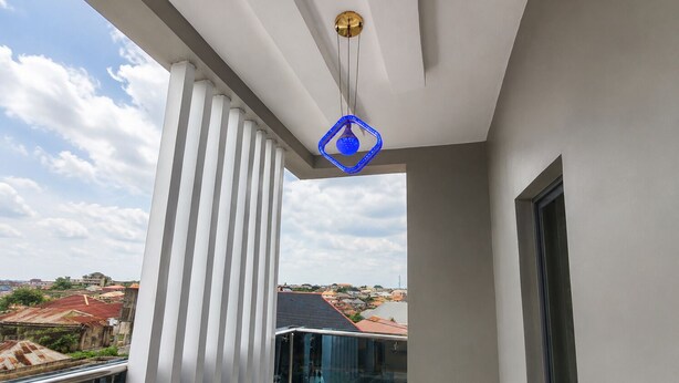 Un balcone con ringhiera in vetro, vista sulla città e una lampada a sospensione blu.