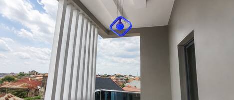 Un balcon doté d’une balustrade en verre, une vue sur le paysage urbain et un luminaire suspendu bleu.