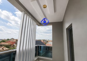 A balcony with a glass railing, a view of the cityscape, and a blue pendant light. - Comfort Peak Apartments (Ibadan)