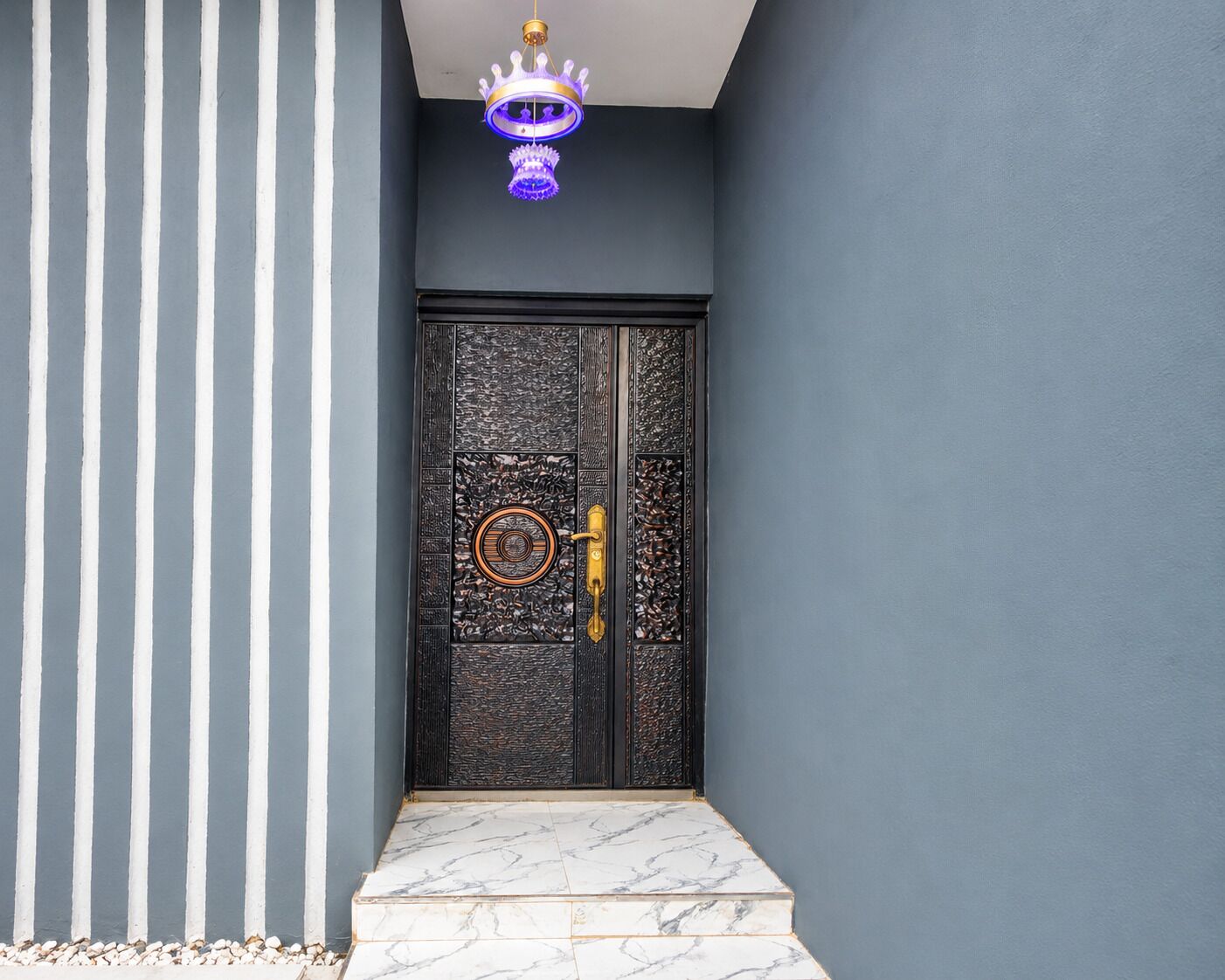 A dark blue door with intricate patterns and a gold handle, leading to a marble staircase.