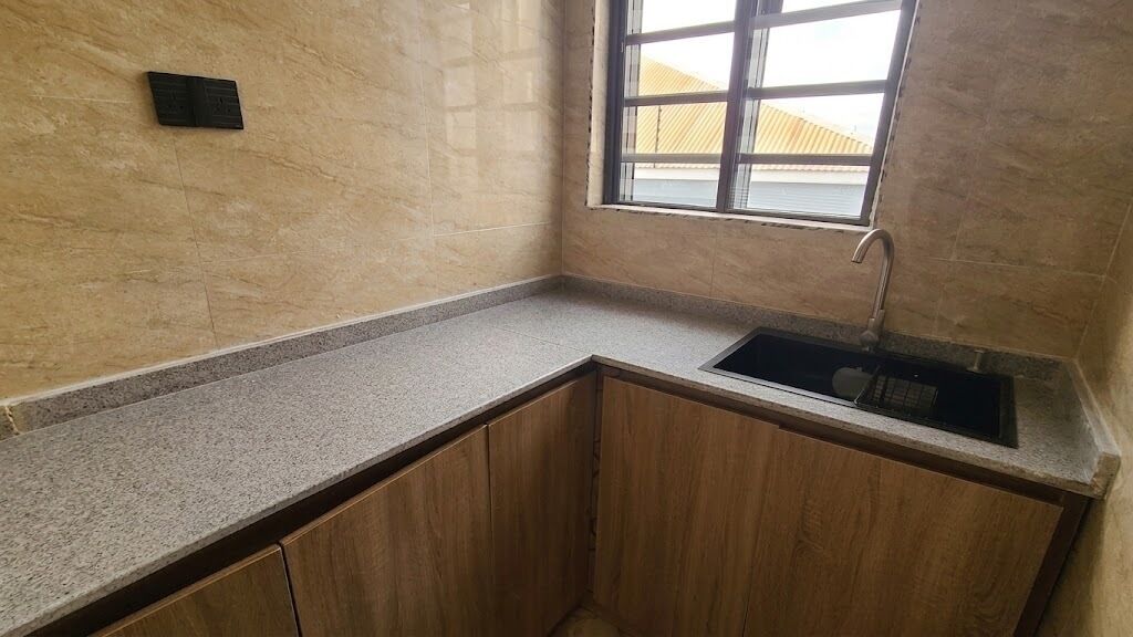 A small kitchen with a granite countertop, wooden cabinets, a stainless steel sink, and a window with a view of a building outside.
