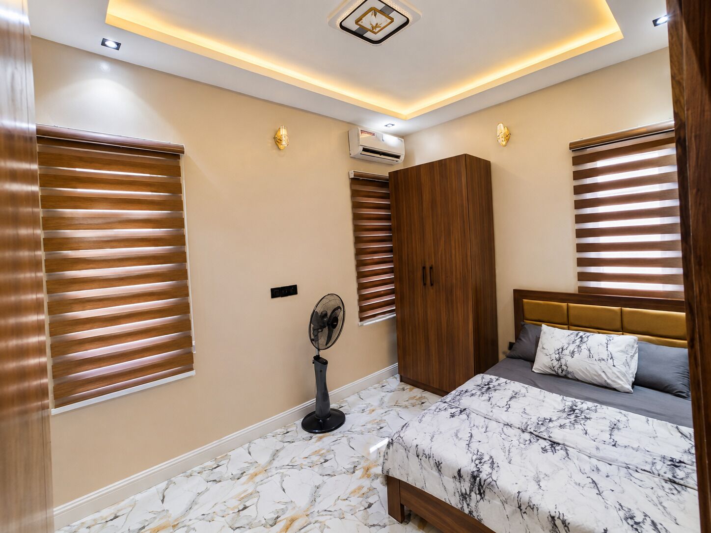 Ein Schlafzimmer mit einem Bett, einem Kleiderschrank, einem Standventilator und einer Deckenleuchte.