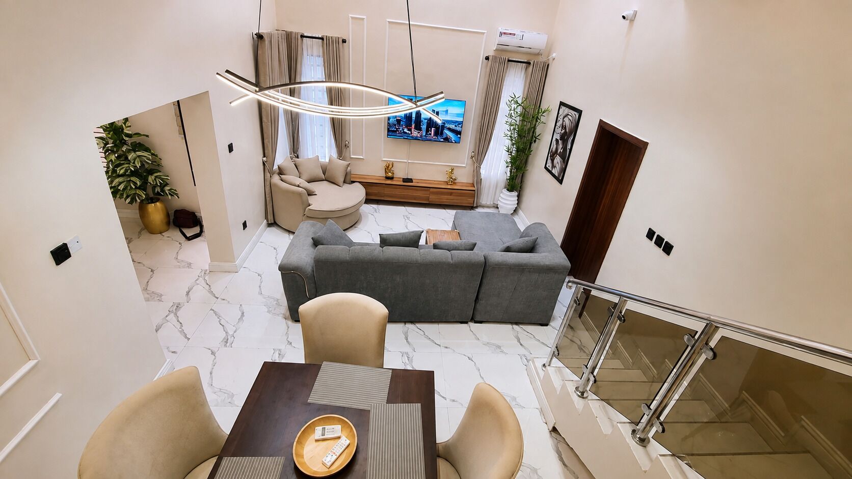 A modern living room with a sofa, a dining table with chairs, a TV, and a staircase.