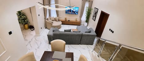 A modern living room with a sofa, a dining table with chairs, a TV, and a staircase.