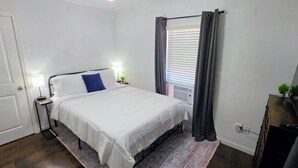 A bedroom with a bed, bedside tables, a lamp, a window with curtains, a radiator, and a TV on a stand.