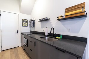 Una cocina moderna con encimera negra, pileta de acero inoxidable y estantes de madera.