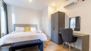 Una camera d'albergo con un letto, comodino, panca, scrivania e sedia, e un condizionatore d'aria.