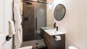 Un bagno moderno con doccia vetro, uno specchio rotondo, un lavandino bianco e un water.
