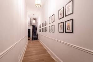 A hallway with a staircase, white walls, and framed pictures on the wall. - Spruce Villa - 3rd Floor King Studio w/ Desk (Philadelphia)