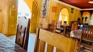Una habitación con paredes y puertas de madera, una cama con colcha estampada, una zona de comedor con sillas y una mesa, y un cuadro en la pared.