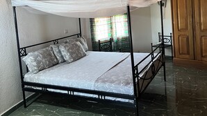 Una cama con dosel y pilares, un armario de madera y suelo de baldosas.