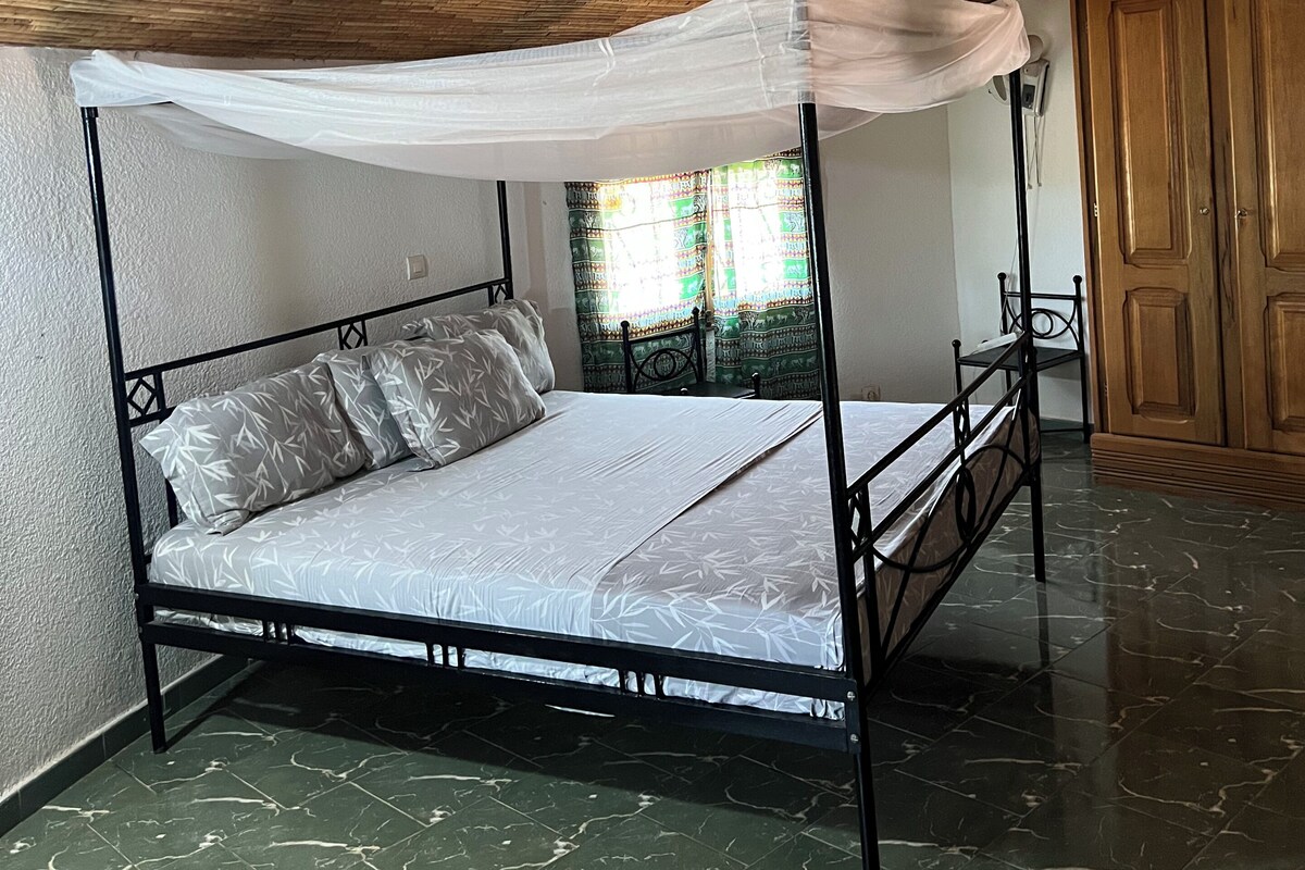 Una cama con dosel y pilares, un armario de madera y suelo de baldosas.