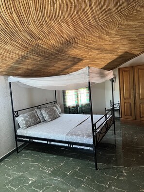 Una cama con dosel y pilares, un armario de madera y suelo de baldosas.