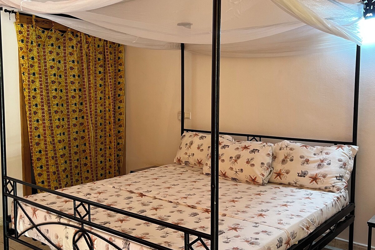 Una cama con dosel y cuatro columnas, un edredón estampado y almohadas a juego.