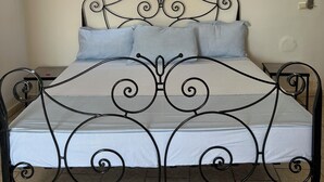 Una cama con estructura metálica y colchón blanco, dos lámparas fijadas a la pared y un equipo de aire acondicionado en la pared.