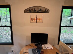 A room with a desk, laptop, and a monitor. There are two windows with a view of trees. - Cozy 1-bedroom cabin in charming Grand Junction with AC (Grand Junction)