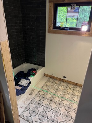 A bathroom with a black tiled shower, a window with an American flag, and patterned floor tiles. - Cozy 1-bedroom cabin in charming Grand Junction with AC (Grand Junction)