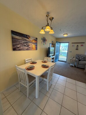 A dining area with a white table and chairs, a painting on the wall, and a ceiling light fixture. - NEW! Surf City 2BR Beach Escape Walk Everywhere Labor Day Available (Surf City)