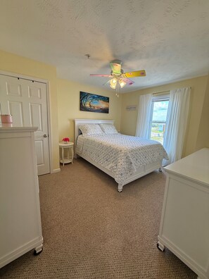 A bedroom with a bed, a ceiling fan, a window with curtains, a door, and a painting on the wall. - NEW! Surf City 2BR Beach Escape Walk Everywhere Labor Day Available (Surf City)