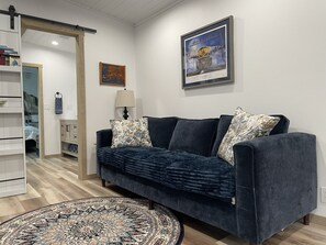 A modern living room with a dark blue sofa, patterned rug, and a framed picture of a train on the wall. - Railroad Retreat in Moose Pass – Car 0037 (Moose Pass)