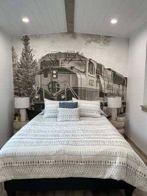 Ein Schlafzimmer mit einem Bett, einem Wandbild mit einem Zug und zwei Nachttischlampen.
