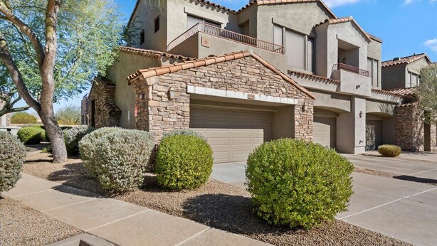 A multi-story house with a garage, surrounded by well-maintained landscaping and a clear sky. - Grayhawk 2BR Condo, Private Garage, Balcony with pool and gym access (Scottsdale)