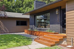 A modern house with a stone facade, a large window, and a wooden deck with steps leading to the entrance.