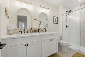 Ein Badezimmer mit einem Doppelwaschtisch, einer Toilette, einer Dusche mit Glastür und einem gerahmten Bild an der Wand.