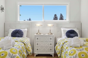 Quarto com duas camas, uma mesa de cabeceira e janela com vista para árvores.