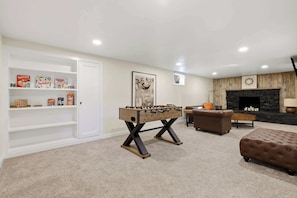 A living room with a foosball table, a brown leather sofa, a coffee table, and a bookshelf with board games.
