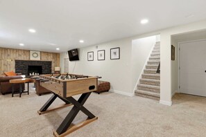 Uma sala de estar com mesa de futebol, lareira, sofá e escada.