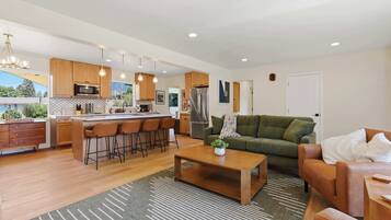 A modern kitchen with wooden cabinets, a central island with bar stools, a green sofa, and a coffee table.