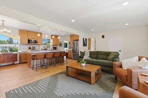 A modern kitchen with wooden cabinets, a central island with bar stools, a green sofa, and a coffee table.