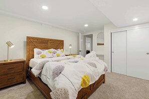 Een slaapkamer met een houten bed, witte beddengoed, een nachtkastje, een lamp en een kledingkast.