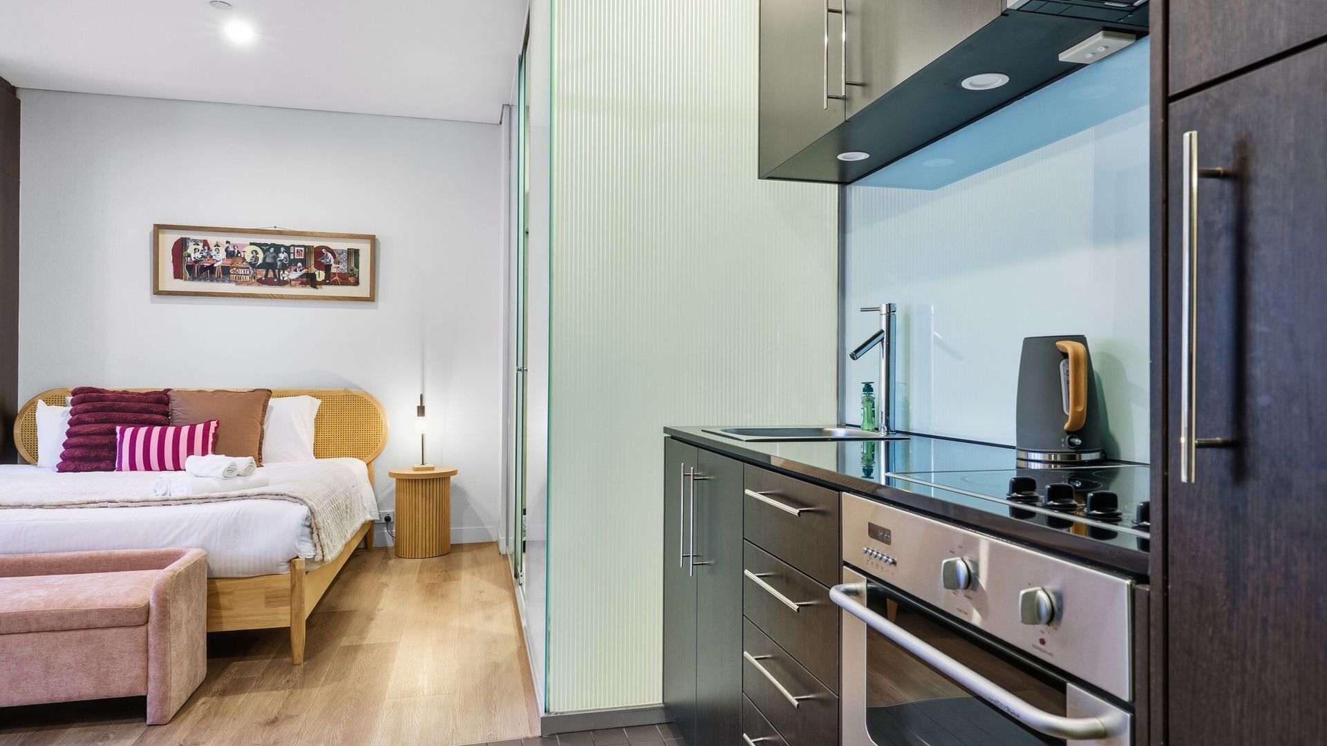 Een moderne hotelkamer met een bed, nachtkastje en een kitchenette.