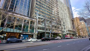 A city street with tall buildings, parked cars, and a clear sky. - Republic Apartment on Collins (Melbourne)