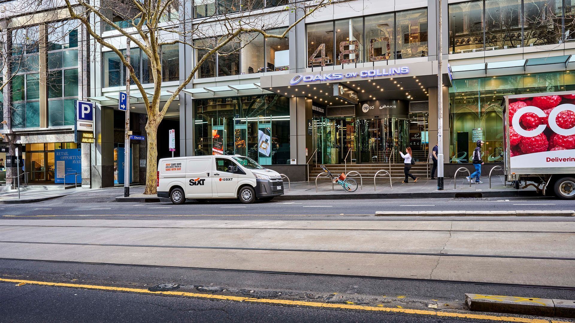 A modern building with a glass facade, a visible storefront for Oakson Collins, and a parking sign.