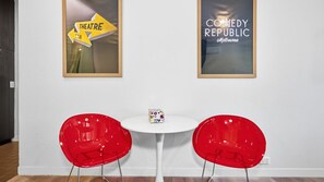 A room with two red chairs, a small white table, and two framed posters on the wall. - Republic Apartment on Collins (Melbourne)