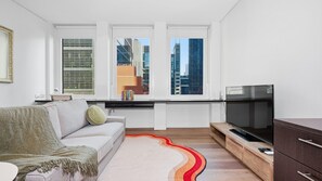 A modern living room with a sofa, a television, and a view of city buildings through large windows. - Republic Apartment on Collins (Melbourne)