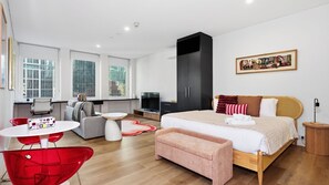 A modern hotel room with a bed, a television, a sofa, a red chair, and a painting on the wall. - Republic Apartment on Collins (Melbourne)