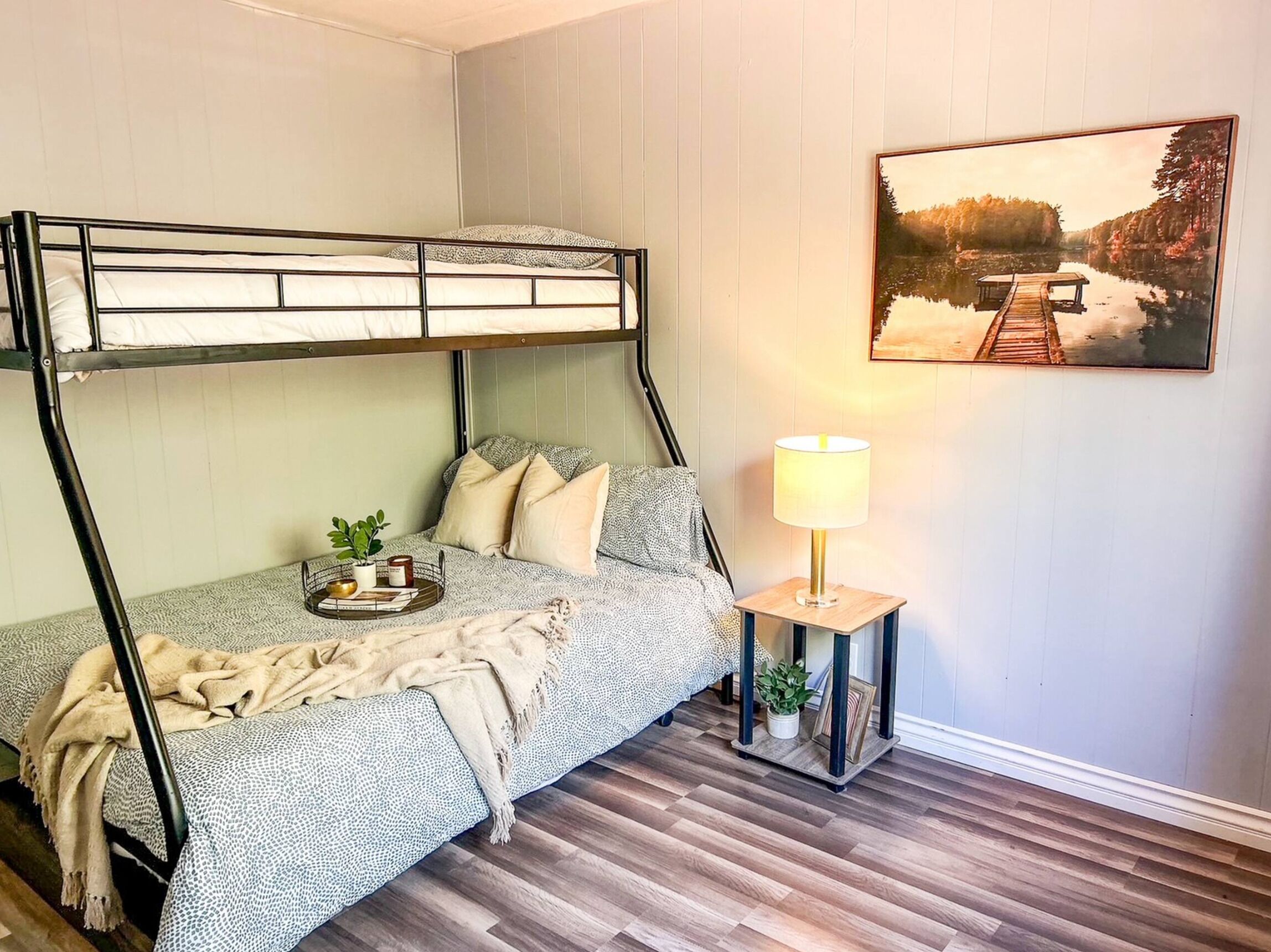 Ein Stockbett mit Nachttisch und Lampe, ein Gemälde eines Sees und ein Holzboden.